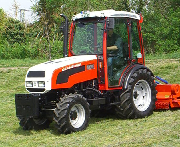 Weiß-roter Traktor am Waldrand Traktor beim Arbeitseinsatz auf Grünfläche